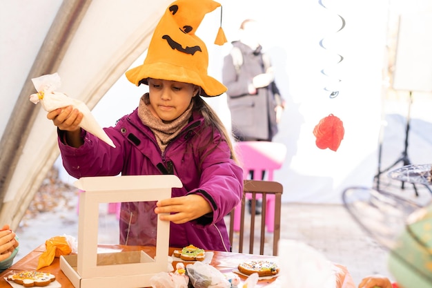Kleine Kinder auf einer Halloween-Party. Kleines Mädchen dekoriert Kekse für Halloween.