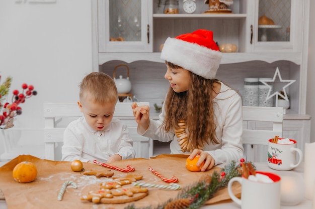 Kleine Kinder, Bruder und Schwester in einer Weihnachtsmütze bereiten Kekse in der Küche zu Hause zu