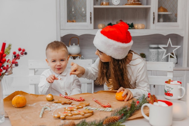 Kleine Kinder, Bruder und Schwester in einer Weihnachtsmütze bereiten Kekse in der Küche zu Hause zu