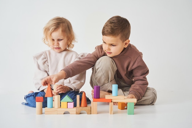 Kleine Kinder Bruder und Schwester lächelnd Spaß haben und spielen farbige Ziegel Spielzeug auf weißem Hintergrund Kinder haben ein Lächeln auf den Lippen und haben Spaß zusammen