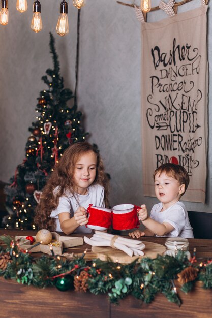 Foto kleine kinder in der weihnachtsdekoration mit tee im gemütlichen haus mit bunten neujahrslichtern