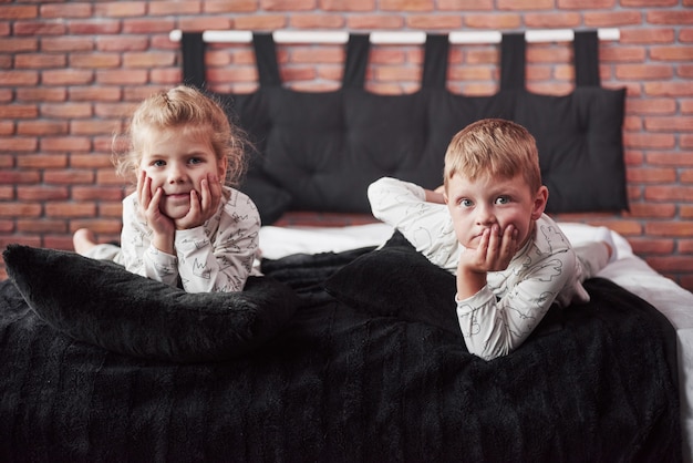 Kleine Kinder, Jungen und Mädchen, die mit Kissen auf der Bettdecke mit einer Decke liegen und spielen