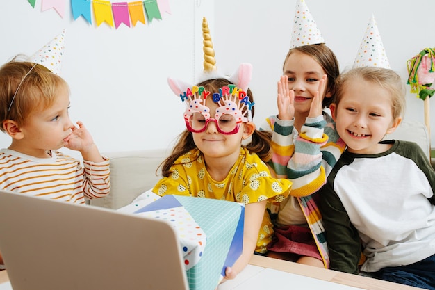 Kleine Kinder mit Partyhüten versammelten sich um einen Laptop, um per Videoanruf zu chatten