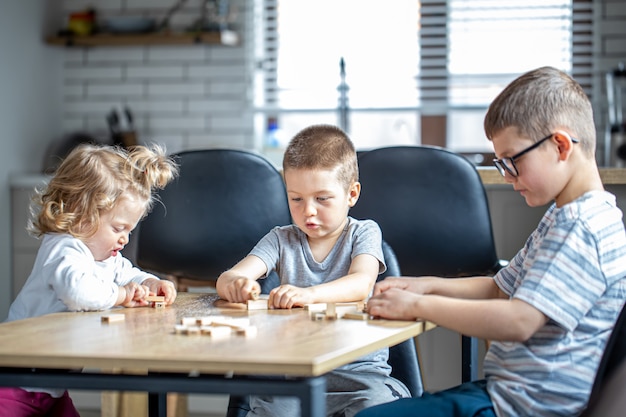 Kleine Kinder spielen zu Hause in der Küche ein Brettspiel mit Holzwürfeln.