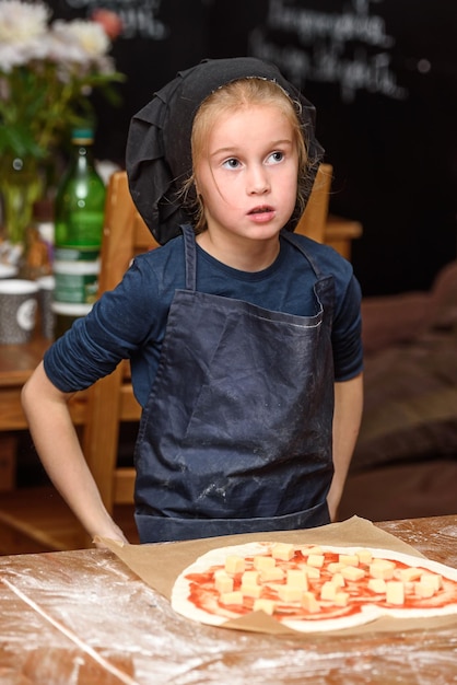 Kleine Köchin in Uniform bereitet Pizza in der Küche zu