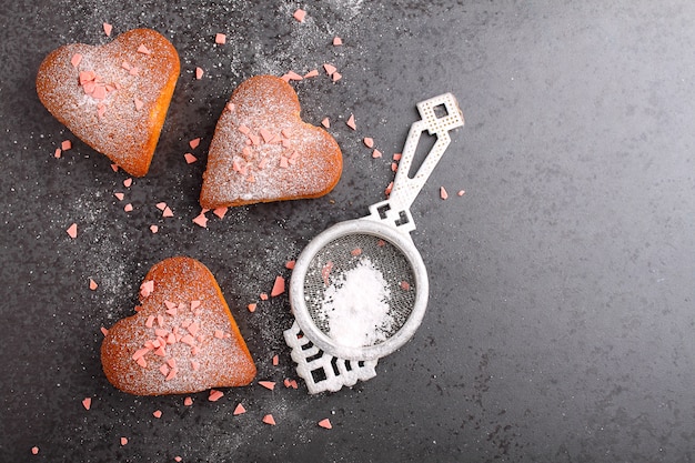 Kleine Kuchen im Herzen mit Puderzucker auf einem schwarzen Hintergrund