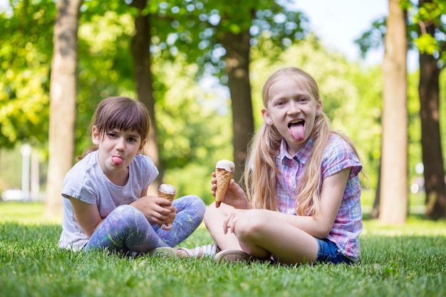 Kleine lächelnde Mädchenfreundinnen, die auf dem Rasen sitzen und Eiscreme essen. Kinderferien