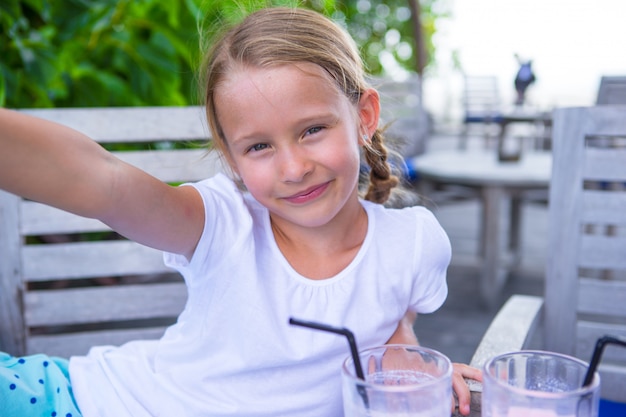 Kleine Mädchen, die selfie nehmen und geschmackvolle Cocktails Café am im Freien trinken