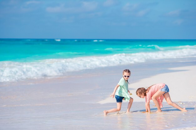 Kleine mädchen, die spaß am tropischen strand zusammen spielt am seichten wasser haben