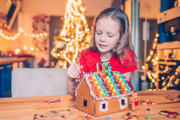 Kleine Mädchen, die Weihnachtslebkuchenhaus am Kamin in verziertem Wohnzimmer machen.