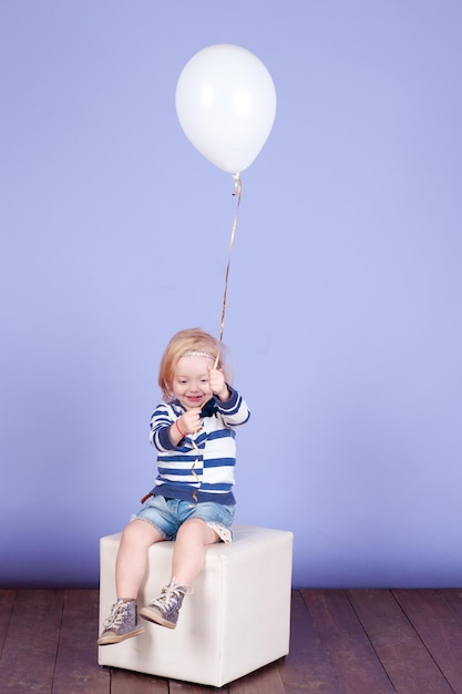 Kleine Mädchen mit Ballon tragen trendige Kleidung über blauem Innenbereich