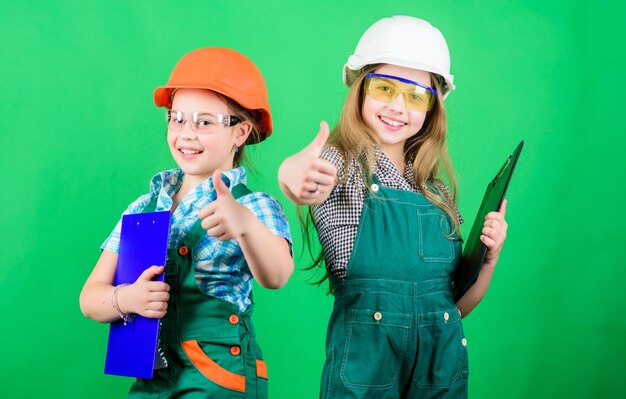 Kleine Mädchen reparieren gemeinsam in der Werkstatt Teamwork-Geschäft Kleine Kinder im Helm mit Tablet Tag der Arbeit 1. Mai Vorarbeiter-Inspektor Reparatur Selbstbewusster Mechaniker bei der Arbeit bestes Team aller Zeiten