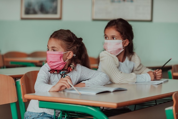 Kleine Mädchen sitzen an Schulbänken und tragen eine Maske gegen den Schutz vor pandemischem Corona-Virus Neue normale Bildung während der Covid19-Pandemie Selektiver Fokus Foto in hoher Qualität