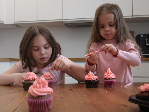 Kleine Mädchen verzieren Cupcakes mit bunten kulinarischen Streuseln
