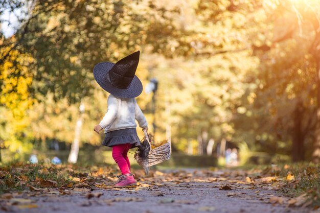 Kleine Mädchenhexe geht mit einem Korb voller Blätter in den Herbstwald.