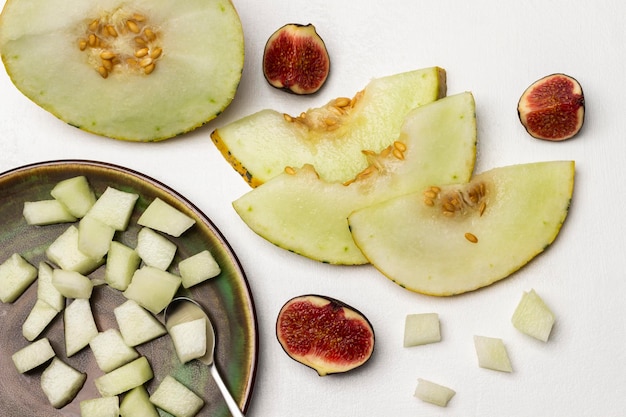 Kleine Melonenstücke und ein Löffel auf einem Teller. In Scheiben geschnittene Melonen- und Feigenhälften