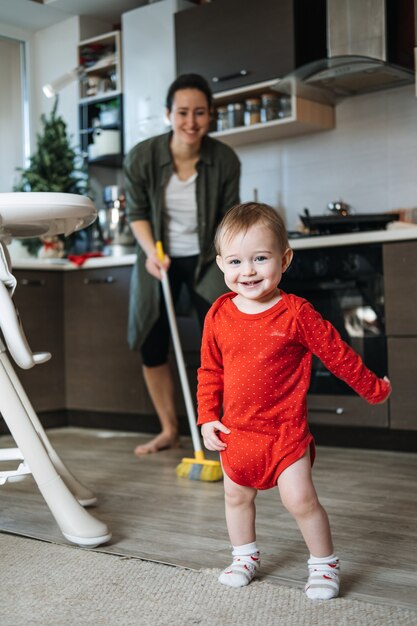 Kleine Mütter Helfer süßes Kleinkind Baby Mädchen mit Mopp helfen ihrer Mutter bei der Hausarbeit in der Küche süß