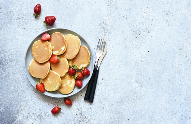 Kleine Pfannkuchen mit Beeren auf einem Teller auf Betonhintergrund Ansicht von oben