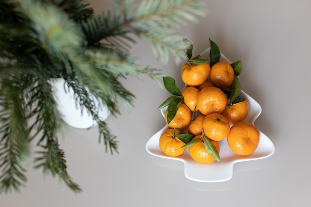 Foto kleine reife mandarinen mit blättern, auf teller in form von weihnachtsbaum auf beigem hintergrund. konzept wintervitaminnahrung. moody stillleben festliche komposition. für grußkarten, bücher, geschichten.