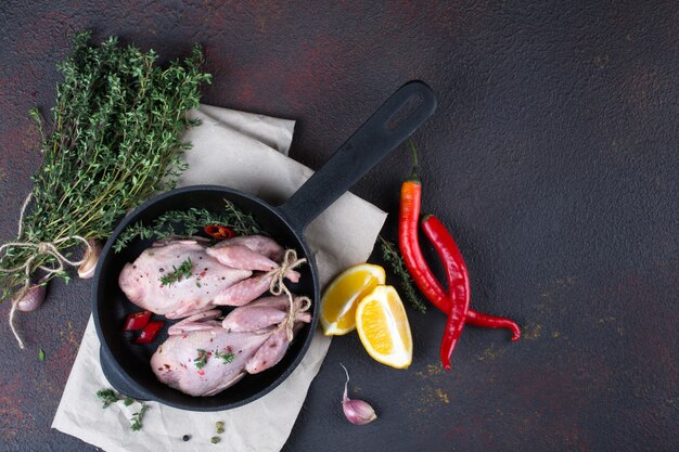 Kleine rohe Quals mit etwas Gewürz zum Kochen auf schwarzer runder Pfanne.