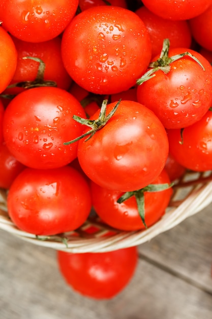 Kleine rote Tomaten in einem Weidenkorb auf einem alten Holztisch. Reife und saftige Kirsche