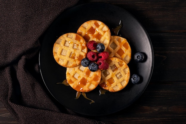 Kleine runde Waffeln, serviert mit Blaubeeren, Himbeeren und Karamellsauce oder Honig, flach gelegt