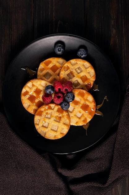 Kleine runde Waffeln serviert mit Heidelbeeren, Himbeeren und Karamellsauce oder Honig. Platz kopieren.