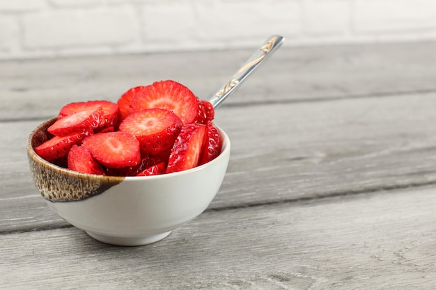 Kleine Schüssel mit Erdbeeren, die mit einem Löffel in kreisförmige Stücke geschnitten werden - bereit, einen gesunden Snack zu essen.