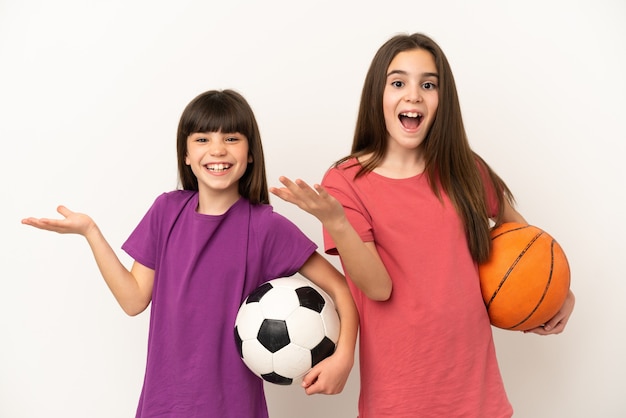 Kleine Schwestern, die Fußball und Basketball spielen, isoliert auf weißem Hintergrund mit Überraschung und schockiertem Gesichtsausdruck