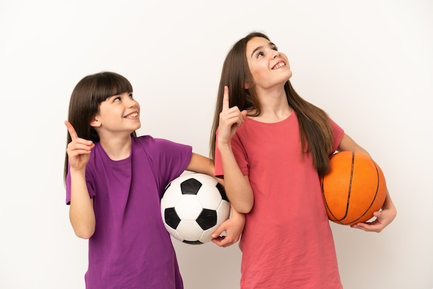 Kleine Schwestern, die isoliert Fußball und Basketball spielen, zeigen mit dem Zeigefinger eine großartige Idee