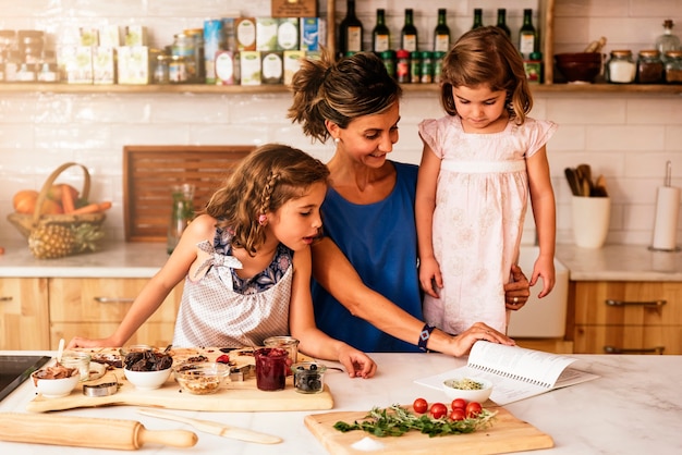 Kleine Schwestern kochen mit ihrer Mutter in der Küche. Konzept des Säuglingskochs.