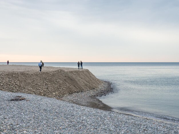 Kleine Silhouetten von Menschen am Ufer Menschen in der Ferne stehen und schauen auf das Meer Bewölktes Wetter Außerhalb der Saison im Schwarzen Meer Resort