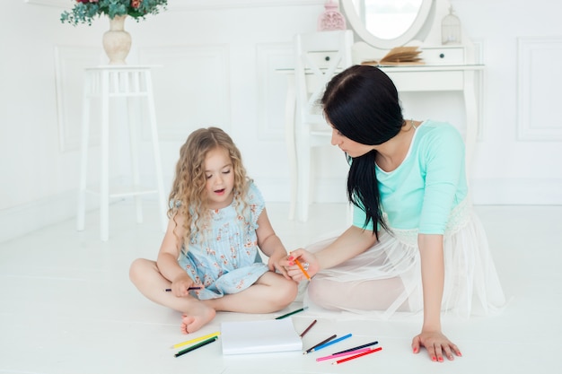 Kleine süße Tochter und ihre Mutter zeichnen mit bunten Stiften und haben Spaß zusammen. Hübsches Kind und Mutter spielen drinnen. Glückliche Familie, die Zeit durch Zeichnen verbringt.