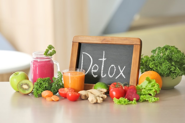 Kleine Tafel mit Wort DETOX, frischen Säften und Zutaten auf dem Tisch