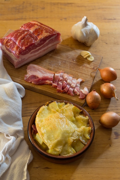 Kleine Tartiflette neben dem Schneidebrett mit Schweinebauch