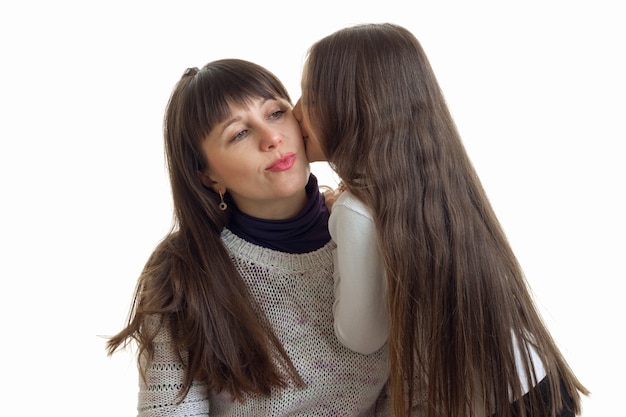 Kleine Tochter, die ihre Mutter auf die Wange küsst, isoliert auf weißem Hintergrund