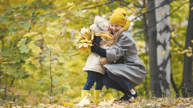 Kleine Tochter mit ihrer Mama spielt mit gelben Blättern im Herbstpark