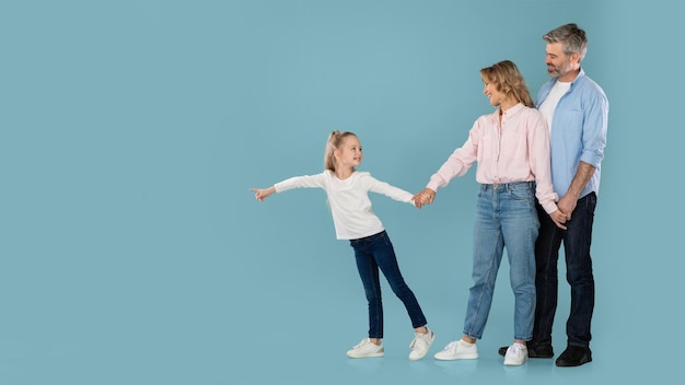 Kleine Tochter zeigt mit dem Finger Händchen haltend mit den Eltern auf blauem Hintergrund