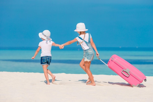 Kleine Touristenmädchen mit großem Koffer am tropischen weißen Strand