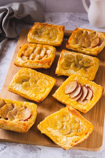 Kleine umgedrehte Blätterteigkuchen mit Banane und Apfel auf einem Brett in vertikaler Ansicht