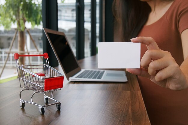 Kleine Warenkorb mit Laptop und Visitenkarte Kopie Raum Bildschirm für Shopping-Online-Konzept.