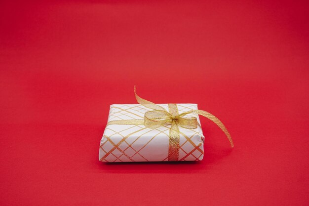 Kleine weiße Geschenkbox mit Goldband. Weihnachtsgeschenkbox. Getrennt auf einem roten Hintergrund