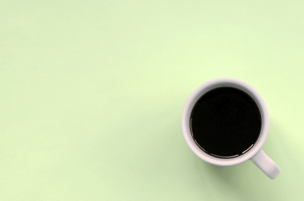 Kleine weiße Kaffeetasse auf Beschaffenheitshintergrund des Modepastellkalk-Farbpapiers