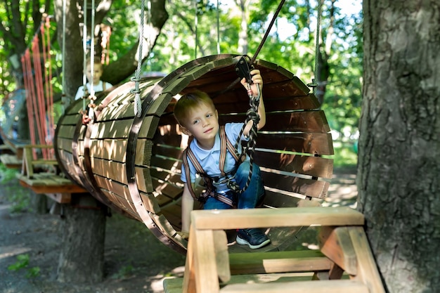 Kleiner aktiver Junge, der im Sommer an einem Seil den Weg zum Vergnügungspark klettert