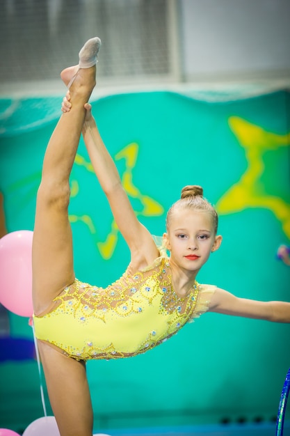 Kleiner aktiver schöner Turner in Wettbewerben der rhythmischen Gymnastik