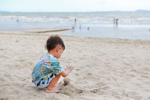 Kleiner asiatischer Junge, der Spaß mit Sand am Strand hat