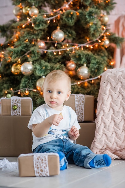 Kleiner blonder Junge, der einen Lebkuchenmann durch den Weihnachtsbaum zu Hause isst.