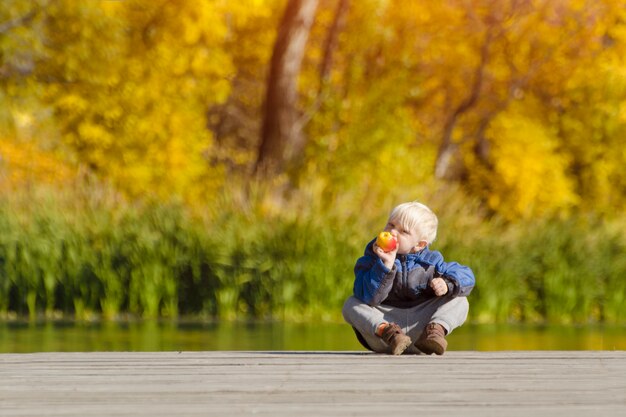 Kleiner blonder Junge einen Apfel auf dem Dock zu essen