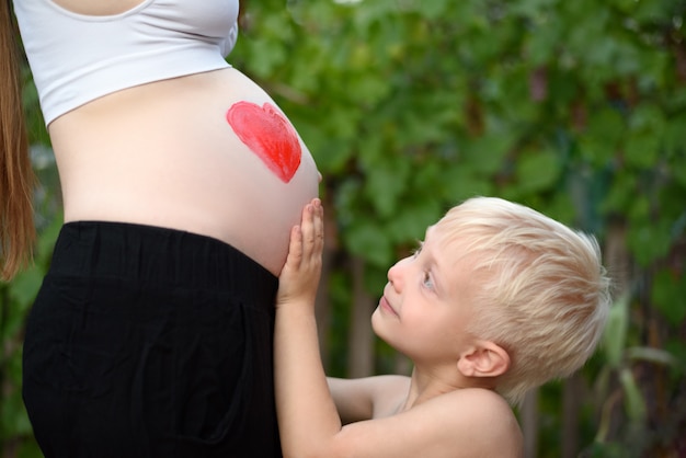 Kleiner blonder Junge streichelt den Bauch seiner schwangeren Mutter. Familie