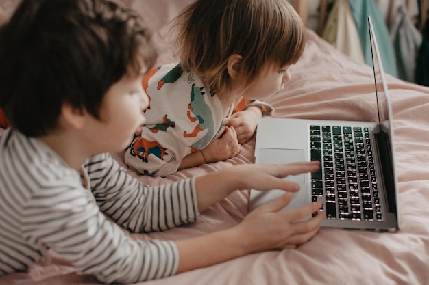 Kleiner Bruder und Schwester liegen im Schlafzimmer auf dem Bett und schauen auf das Laptop ein Foto in hoher Qualität